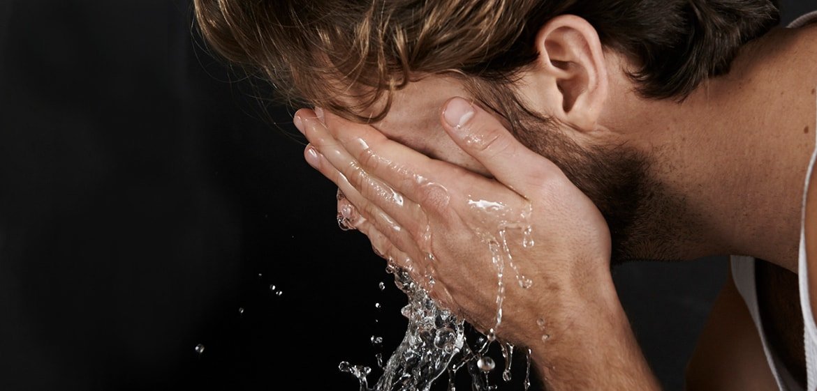 Brünetter Mann wirft sich Wasser aus seinen Handflächen ins Gesicht